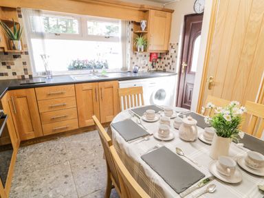 A kitchen with wooden cabinets a dining table set with cups and plates and a plant on the table at Peters Farmhouse in Cookstown