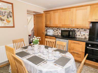 A kitchen with a dining table set for six with cups and cutlery and wooden cabinets with a microwave on the counter at Peters Farmhouse in Cookstown