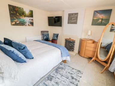 A bedroom with a bed blue pillows a wall-mounted TV a fireplace a wooden dresser with a lamp a stand mirror two paintings and a chair at Peters Farmhouse in Cookstown