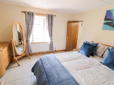 A bedroom with a bed with blue pillows and a blue cover near a window with gray curtains and a wooden dresser at Peters Farmhouse in Cookstown
