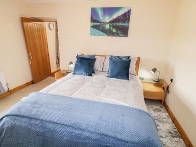 A bedroom with a bed with blue pillows and blanket two wooden nightstands with lamps and a door at Peters Farmhouse in Cookstown