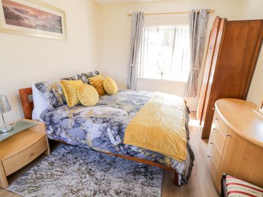 A bedroom with a bed with yellow and grey bedding and pillows with a wooden dresser and wardrobe and window with curtains at Peters Farmhouse in Cookstown