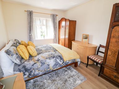 A bedroom with a bed with yellow pillows and a gray patterned duvet a wooden wardrobe a dresser with a mirror a chair and a window with curtains at Peter's Farmhouse in Cookstown