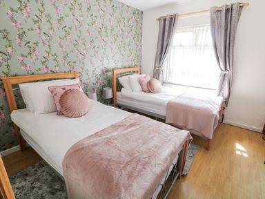 A bedroom with two single beds with pink cushions and throws and floral wallpaper at Peters Farmhouse in Cookstown