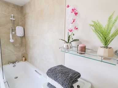 A bathroom with a bathtub a showerhead folded towels and a glass shelf holding a potted plant a candle and an orchid at Peters Farmhouse in Cookstown