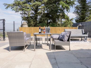 An outdoor patio with two grey wicker sofas with cushions around a table with wine bottles and glasses at Peters Farmhouse in Cookstown