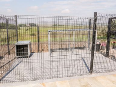 An outdoor fenced area with a dog house and a covered metal cage at Peters Farmhouse in Cookstown