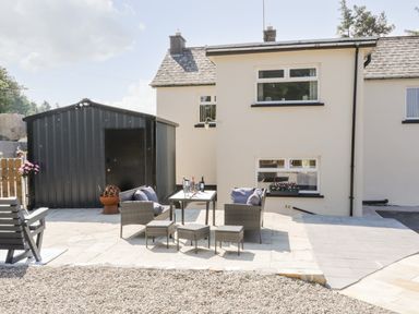 An outdoor patio area with outdoor furniture and a black metal shed behind a white house at Peters Farmhouse in Cookstown