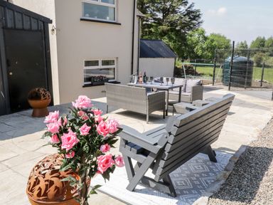An outdoor patio with a wooden bench, grey rattan seating set, pink flowers and a fireplace at Peters Farmhouse in Cookstown