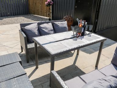 An outdoor patio with a woven table and cushioned chairs with wine bottles and glasses on the table at Peters Farmhouse in Cookstown