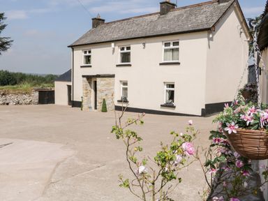 A farmhouse with stone accents and several windows surrounded by a large concrete yard with flowering plants at Peters Farmhouse in Cookstown