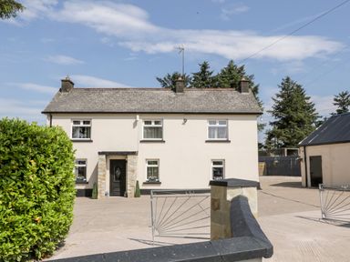 A two-story house with a gated driveway and a hedge at Peters Farmhouse in Cookstown