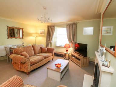 A living room with a patterned sofa a coffee table with fruit a television on a stand and a fireplace at Drake's Retreat in Plymouth