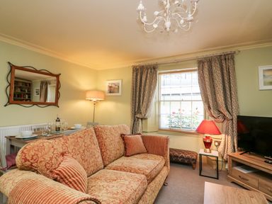 A living room with patterned sofa dining table with wine glasses floor lamp and curtains at Drakes Retreat in Plymouth