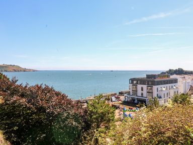A view of the sea with a modern white building and trees in the foreground at Drake's Retreat in Plymouth