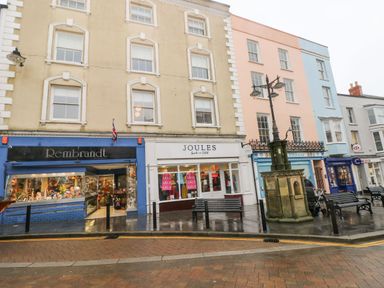 Three story buildings with shops on the ground floor benches and a street lamp in front of them at Gower View in Tenby