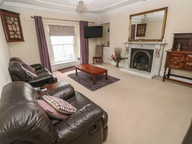 A living room with leather sofas a wooden coffee table a fireplace and a wall-mounted TV at Gower View in Tenby
