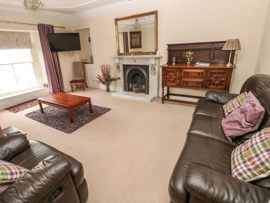 A living room with leather sofas a wooden coffee table a fireplace a large mirror and a wooden sideboard at Gower View in Tenby