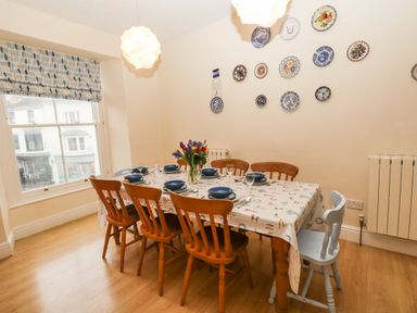 A dining room with a window six wooden chairs a table set with plates and glasses and decorative plates on the wall at Gower View in Tenby