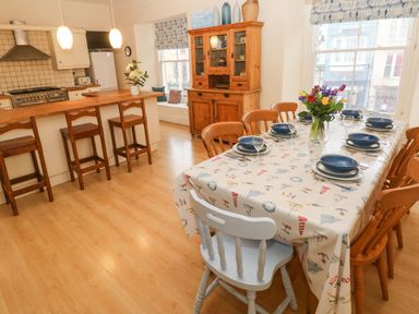 A kitchen and dining area with wooden chairs a table set with plates and glasses and a wooden cabinet at Gower View in Tenby