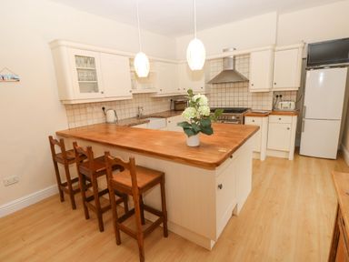 A kitchen with wooden countertop island and three chairs a white refrigerator and stove with hood Gower View Tenby