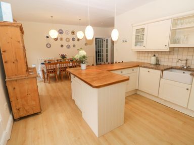 A kitchen with wooden countertops white cabinets a wooden dining table with chairs and decorative plates on the wall at Gower View in Tenby