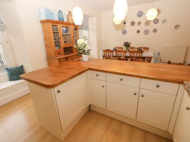 A kitchen island with wooden countertop and white cabinets next to a wooden hutch and a dining table with chairs and plates on the wall at Gower View in Tenby
