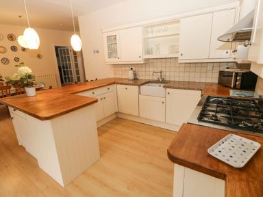 A kitchen with wooden countertops white cabinets a gas stove and a small dining area visible at Gower View in Tenby