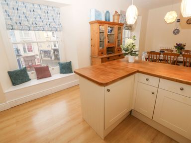 A kitchen with a wooden countertop white cabinets a wooden cupboard and a window seat with cushions at Gower View in Tenby