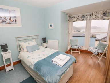 A bedroom with a single bed bedside tables two chairs near a bay window and wooden flooring at Gower View in Tenby