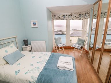A bedroom with a double bed two chairs by the window and mirrored wardrobes at Gower View in Tenby