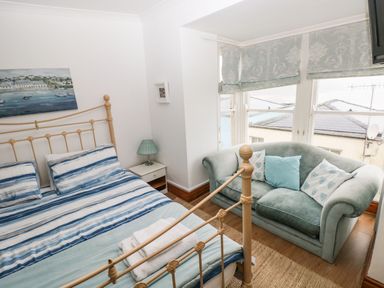 A bedroom with a metal bed frame blue striped bedding a green sofa and windows with patterned blinds at Gower View in Tenby