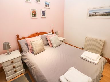 A bedroom with a double bed and pillows two bedside tables with lamps and framed pictures on the walls at Gower View in Tenby