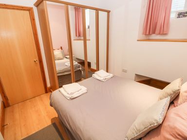 A bedroom with a double bed pillows folded towels a mirrored wardrobe wooden door and window with curtains at Gower View Tenby