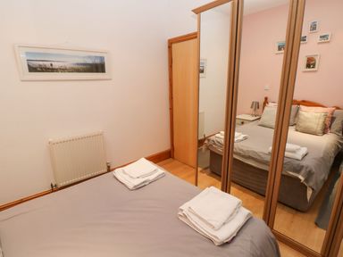 A bedroom with a double bed towels on bed wooden wardrobe with mirrored doors and a closed wooden door at Gower View in Tenby