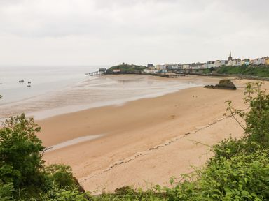 A sandy beach with a few boats in the water and colorful buildings along the coastline at Gower View in Tenby