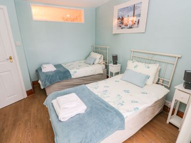 A bedroom with two single beds covered with floral bedding and blue throws with towels on top at Gower View in Tenby