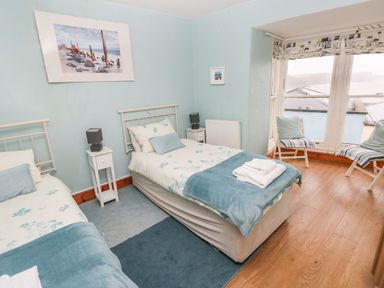 A bedroom with two single beds a window with chairs and cushions and wall art at Gower View in Tenby