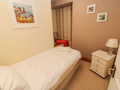 A small bedroom with a single bed beside a window with striped curtains and a bedside table with a lamp at Gower View in Tenby