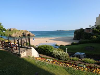 A beach with a rocky island and a garden with flowers and benches at Gower View in Tenby