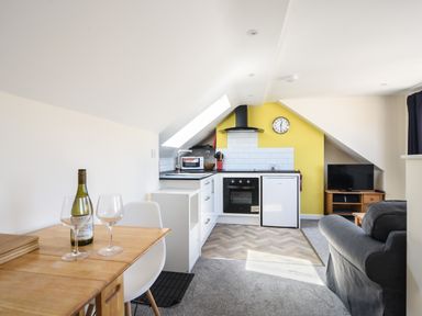 A kitchen and living area with a small dining table bottle of wine and two wine glasses at Ayla in Lyme Regis