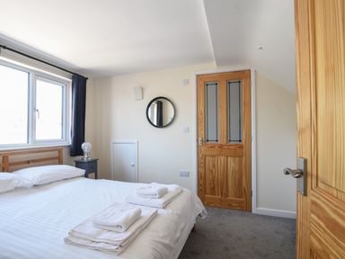 A bedroom with a bed folded towels a bedside table with a lamp round mirror and wooden doors at Ayla Lyme Regis