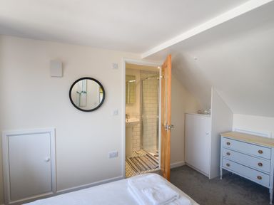 A bedroom with a bed and towels a round mirror a door leading to a bathroom a chest of drawers and a cupboard at Ayla in Lyme Regis