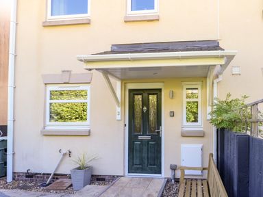 A house entrance with a green front door a covered porch two windows a wooden bench and a potted plant at 3 Trem Y Dolydd in Dolgarrog near Llanrwst