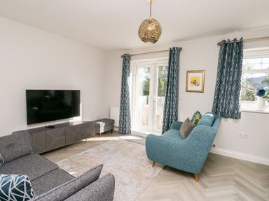 A living room with a wall mounted TV two sofas patterned curtains and glass doors at 3 Trem Y Dolydd in Dolgarrog near Llanrwst
