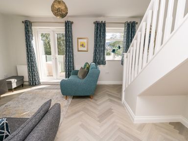 A living room with a teal sofa a gray armchair a rug curtains on windows and a staircase at 3 Trem Y Dolydd Dolgarrog near Llanrwst