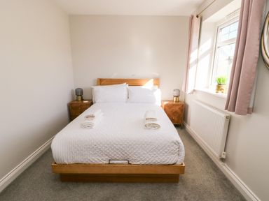 A bedroom with a wooden bed frame white bedding two bedside tables with lamps and a window with curtains at 3 Trem Y Dolydd in Dolgarrog near Llanrwst