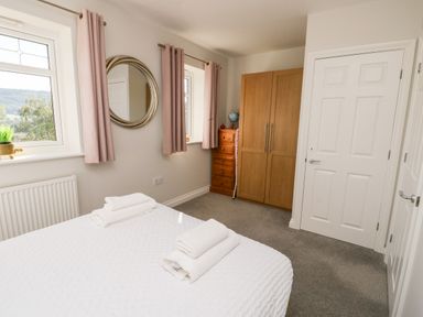 A bedroom with a bed and folded towels near windows with curtains and wooden wardrobe at 3 Trem Y Dolydd Dolgarrog near Llanrwst