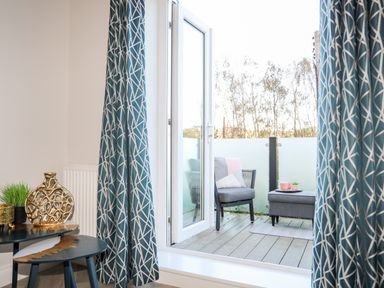 A balcony with a chair and ottoman outside glass doors with patterned curtains at 3 Trem Y Dolydd in Dolgarrog near Llanrwst