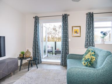 A living room with teal sofa and patterned curtains with doors leading to a balcony at 3 Trem Y Dolydd in Dolgarrog near Llanrwst